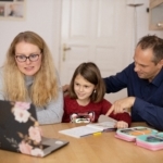 Parents at kitchen table helping elementary girl prepare for school